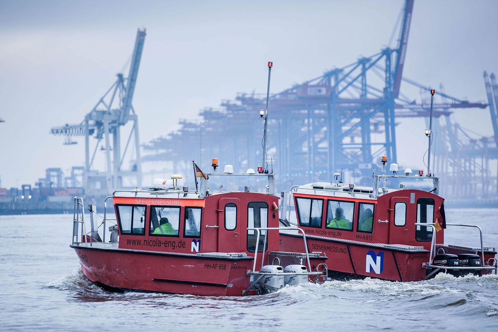 Zwei rote Boote auf See mit einem Hafen im Hintergrund